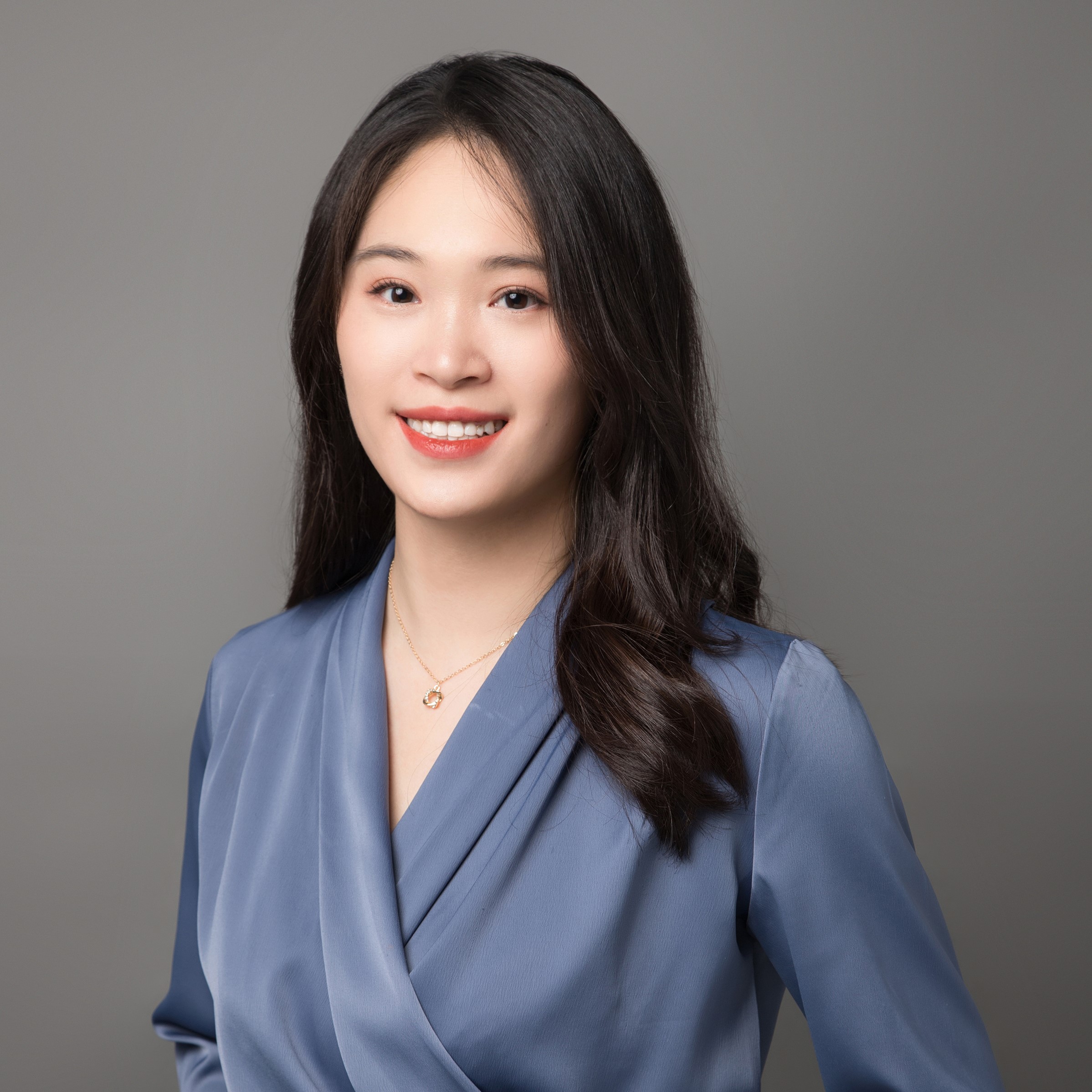Person smiling in a blue blouse against a gray background.