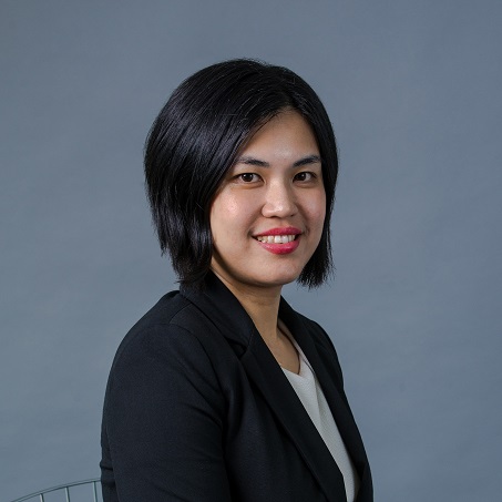 Person in a black blazer smiling at the camera against a gray background.