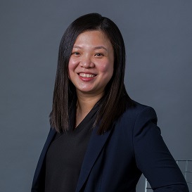 Person smiling with dark hair, wearing a navy blazer and black shirt.