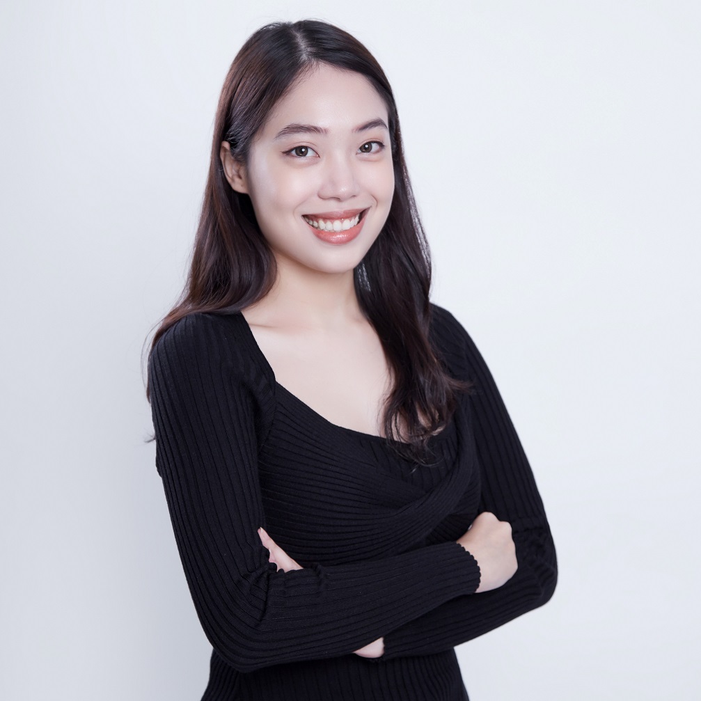 Person smiling with arms crossed, wearing a black top against a light background.