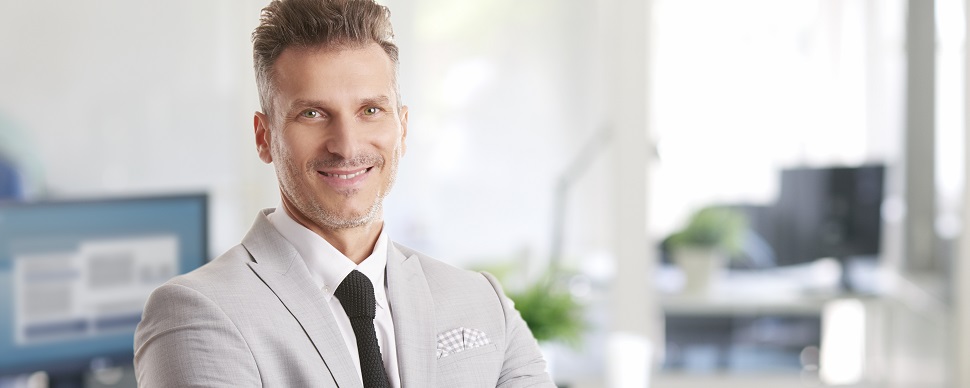 Smiling person in a light gray suit standing in a modern office.