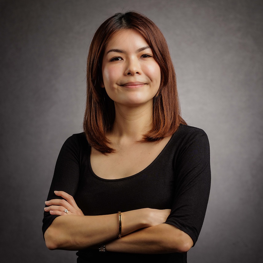 Person smiling with arms crossed, wearing a black shirt, against a gray background.