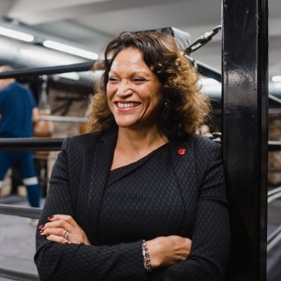 Person smiling in a boxing gym, wearing a dark blazer.