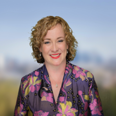 Person with curly hair and a floral top smiling outdoors
