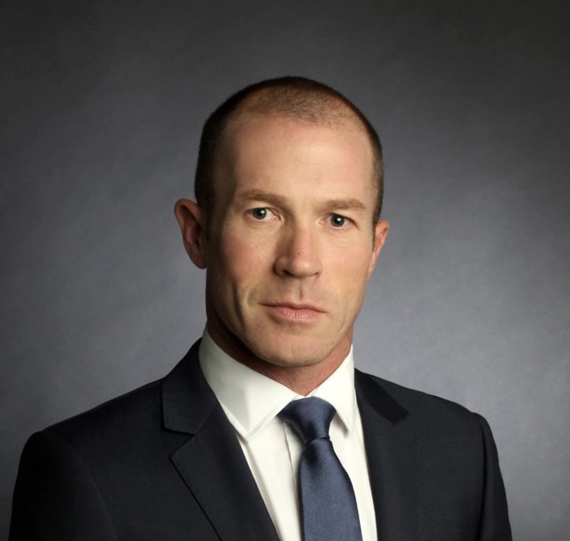 Person in a formal suit against a dark background.