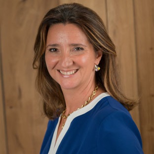 Person with medium-length hair, smiling, wearing a blue top against a wooden background.