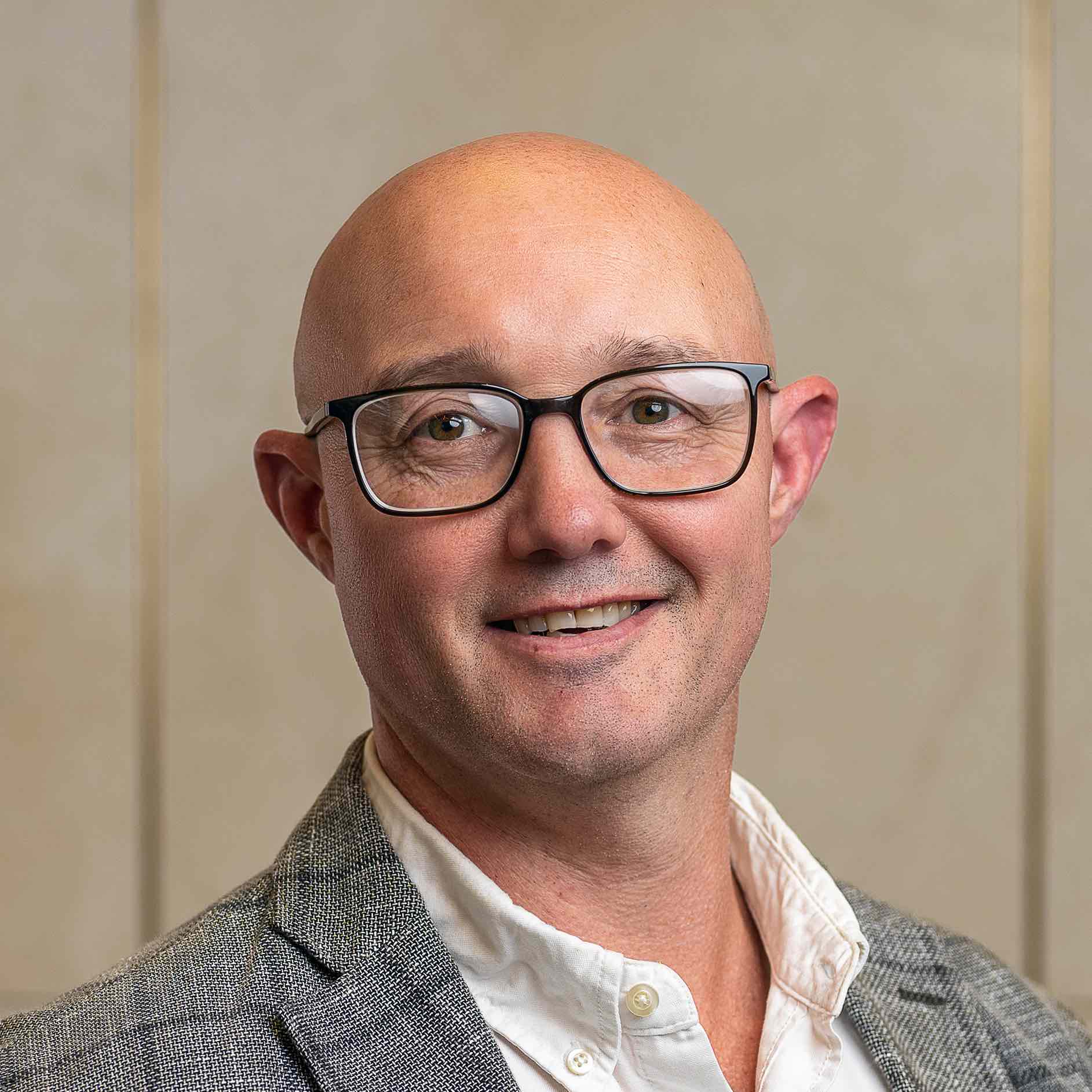 Person wearing glasses and a blazer, smiling indoors.