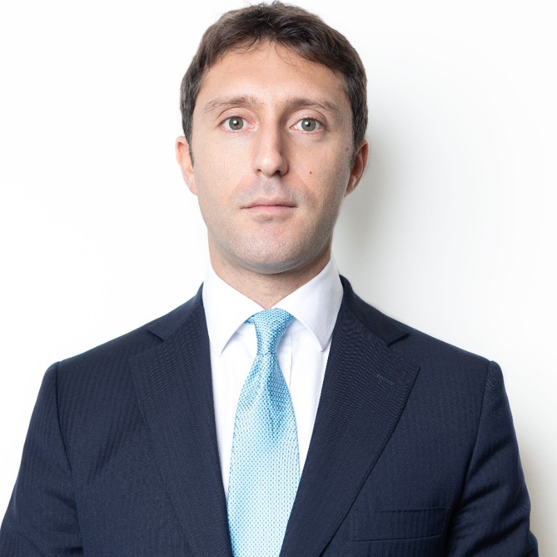 Person in a suit with a blue tie against a white background.