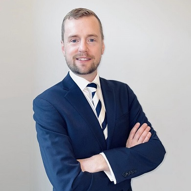 Person in a suit smiling with arms crossed.