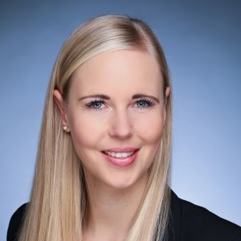 Smiling person with long hair and a professional suit against a blue background.