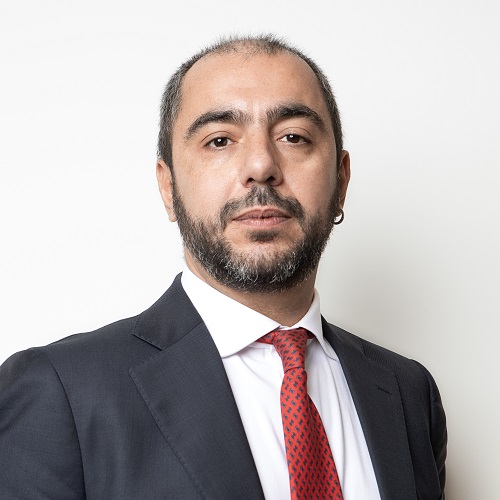 Person in a suit with a red tie, looking at the camera.