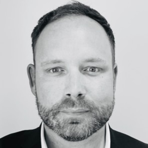 Black and white portrait of a person with short hair, wearing a suit jacket, looking directly at the camera.