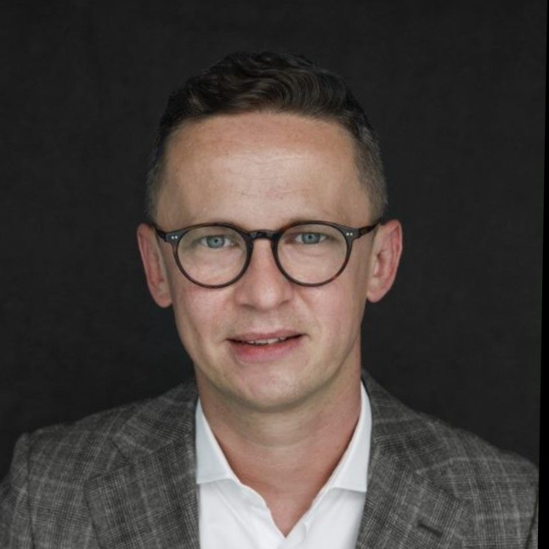 Individual wearing glasses and a suit, smiling at the camera.