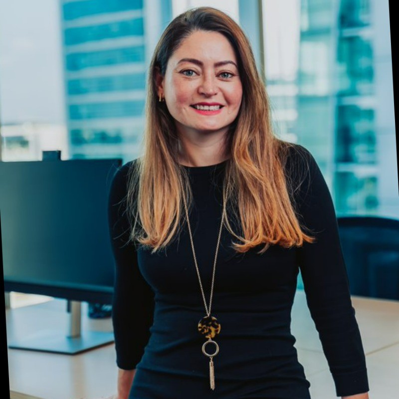 Smiling person in an office with a city view outside the window.