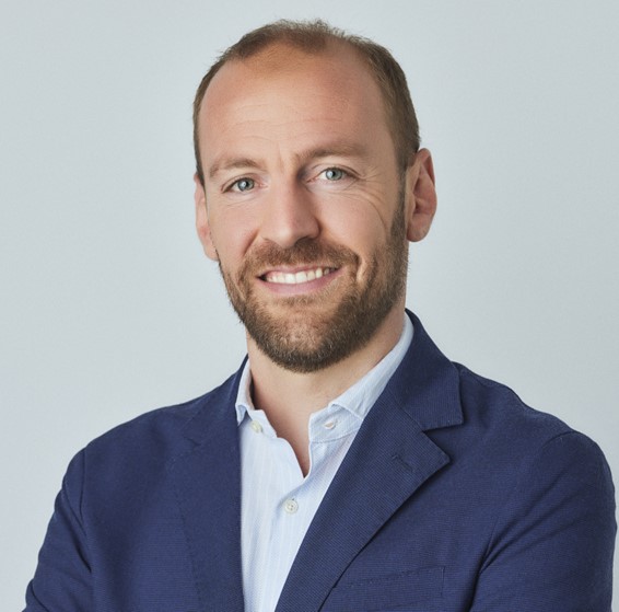 Person in a blue blazer, smiling and standing against a light background.