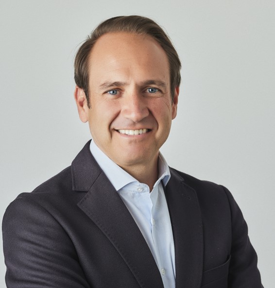 Person in a suit smiling with arms crossed.