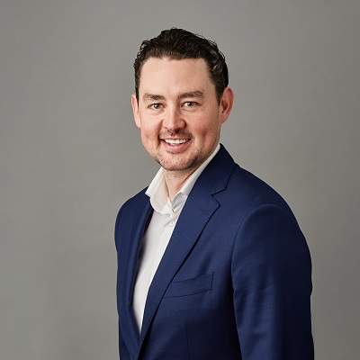 Person in a blue suit smiling against a gray background.