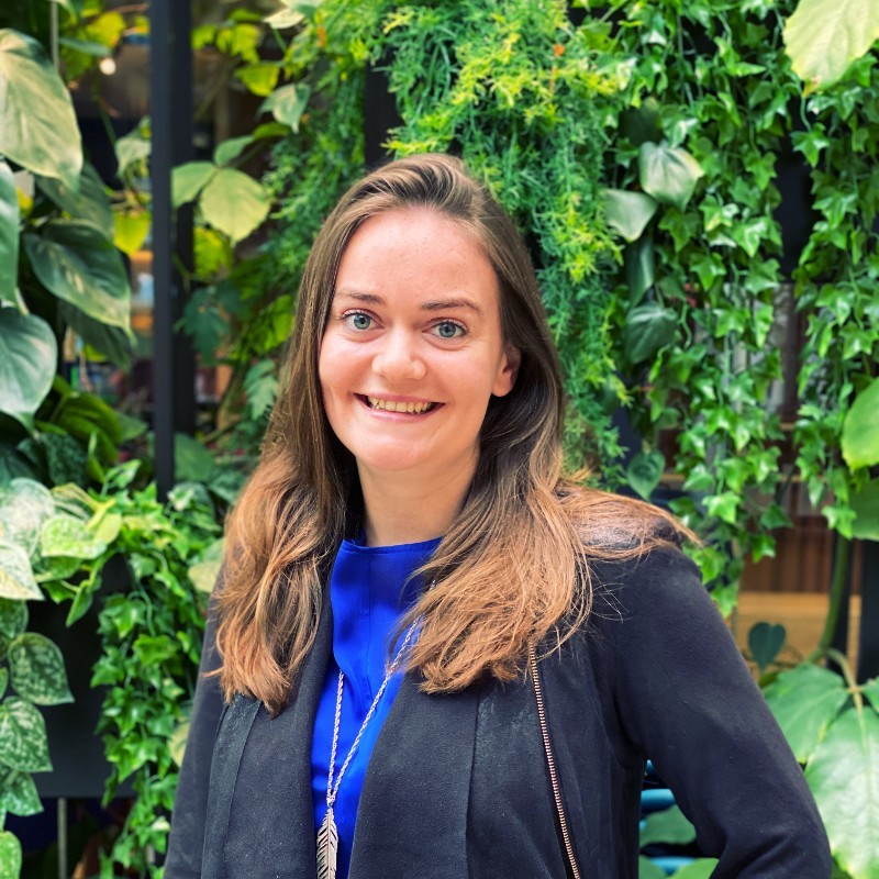 Person smiling in front of a lush green plant background.