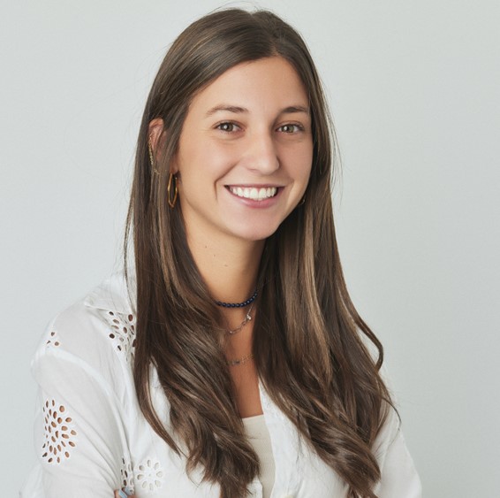 Smiling person with long hair wearing a white blouse.