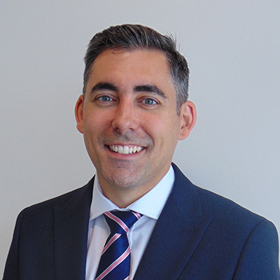 A person in a suit smiling against a plain background.