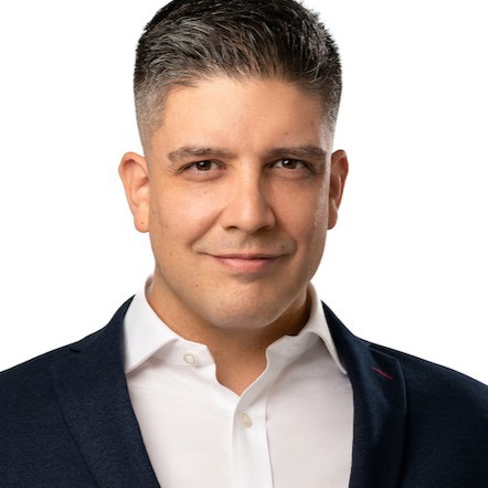 Portrait of a person smiling, wearing a dark suit and white shirt.