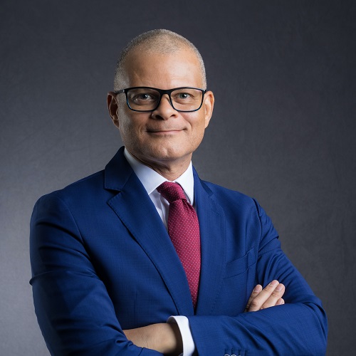 Person in a blue suit and red tie, smiling with crossed arms.