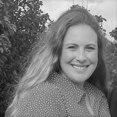 Person smiling outdoors with trees in the background.