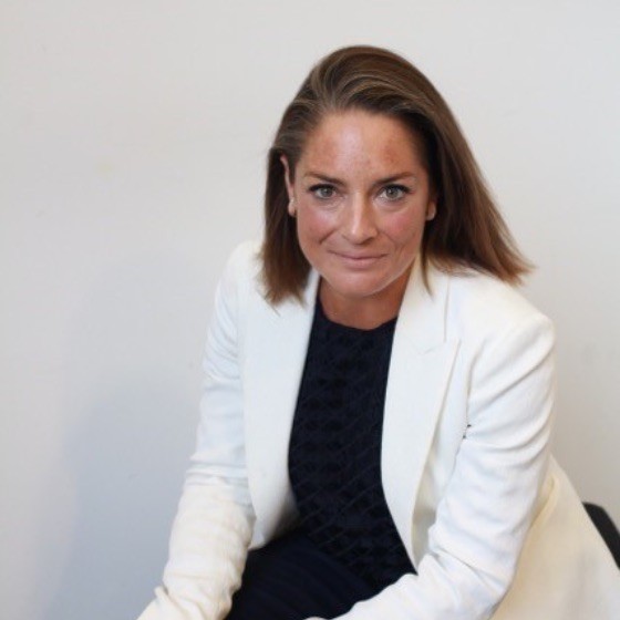 A person in a white jacket sitting and looking at the camera against a plain background.