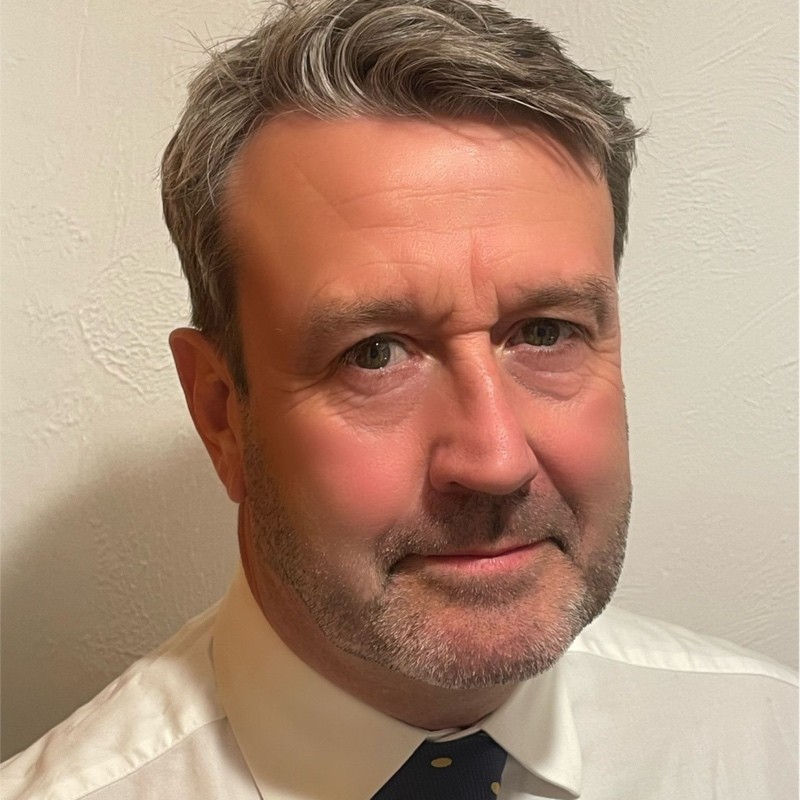 Person wearing a white shirt and dark tie against a textured wall.