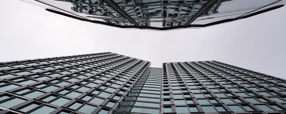 Upward view of mirrored glass skyscrapers against a cloudy sky.
