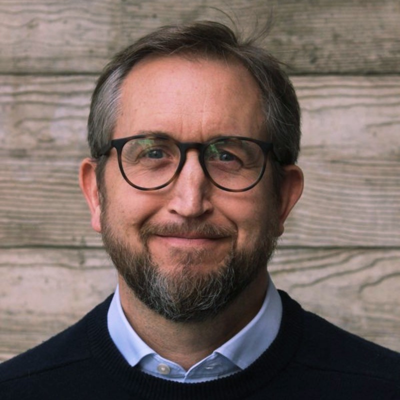 Person smiling with glasses in front of a wooden wall.