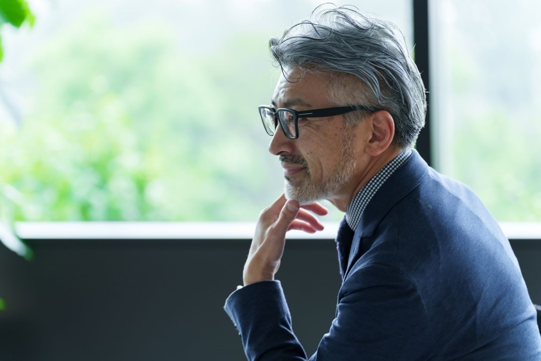 Person with glasses gazing out a window, wearing a blue jacket.