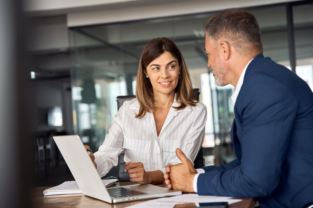 Two people discussing work at a table with a laptop.