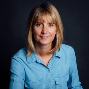 Person in a blue shirt smiling against a dark background.