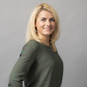 Person smiling in front of a gray background wearing a patterned green shirt.