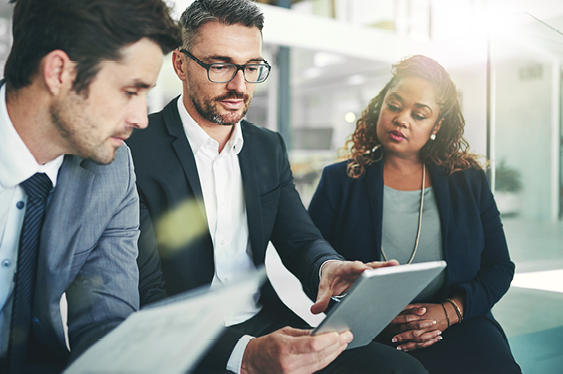 Three people in a business meeting, looking at a tablet.