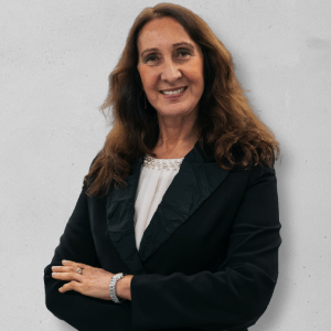 Person smiling, wearing a dark blazer, arms crossed in front of light gray background.