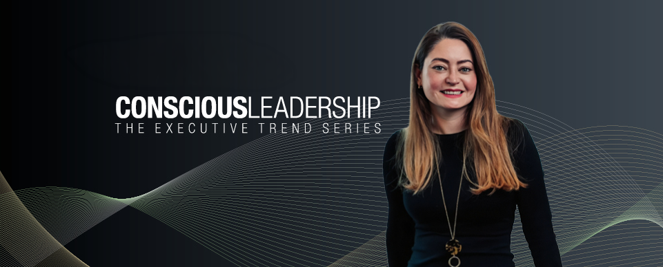 Page Executive Conscious Leadership banner featuring a smiling woman with long blonde hair, wearing a black outfit and a gold necklace, against a dark background with abstract wave patterns.