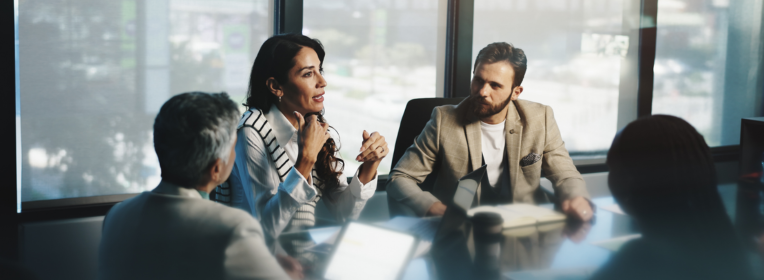 People meeting around a conference table in a modern office, with one person speaking and others listening.