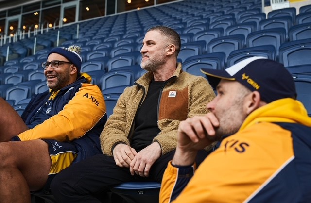 three men sitting in the stands smiling