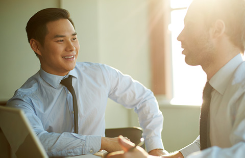 Two people in an office setting discussing at a table with a laptop.