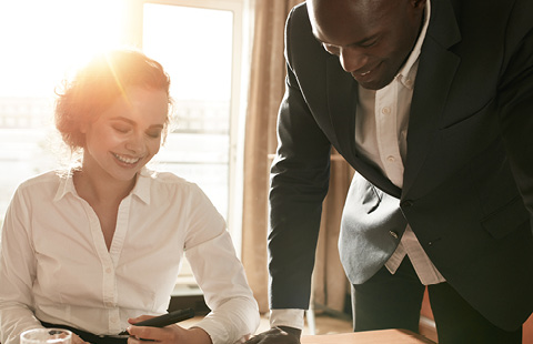 Two colleagues working together at a desk with sunlight streaming through a window.