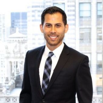 Person in a business suit smiling in an office setting with cityscape view.