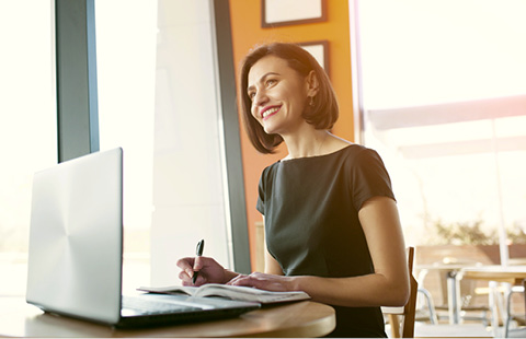 Person smiling while working on a laptop near a window.