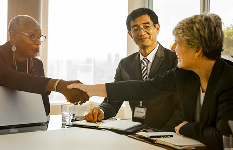 Three people in a meeting room, two shaking hands and smiling.