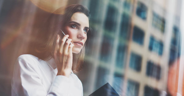 Person looking thoughtful while talking on a phone, standing by a window.