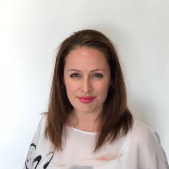 Person with medium-length hair, wearing a light-colored top, smiles against a white background.