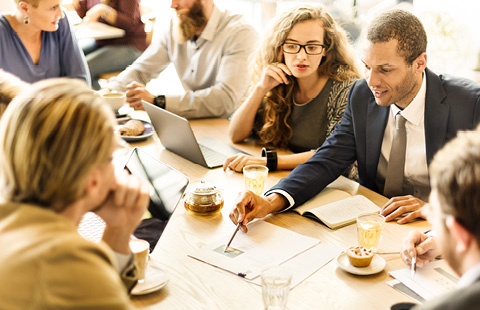 Group of people discussing in a meeting with laptops and notebooks on a table.