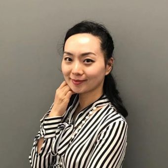 Person in striped shirt smiling against gray background.