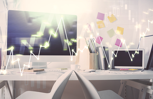 Office with computers displaying graphs, white desks, and colorful sticky notes.